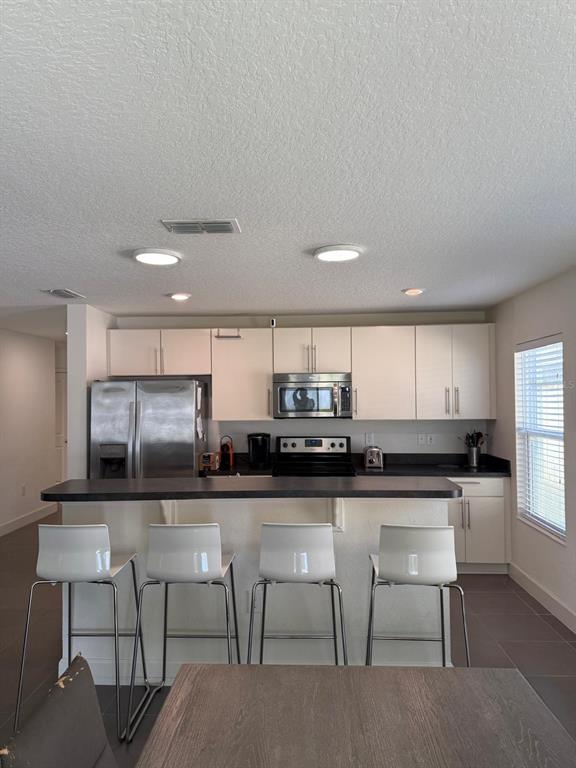 A kitchen features white cabinets, stainless steel appliances, a dark countertop, and four bar stools — 3230 BAYOU LANE, TAVARES, FL