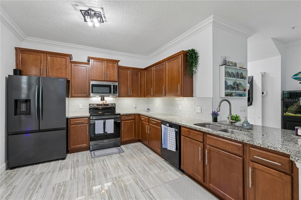 A kitchen features wood cabinets, granite countertops, stainless steel appliances, and light-colored tile flooring — 2264 BETSY ROSS LANE UNIT 2264, ST CLOUD, FL