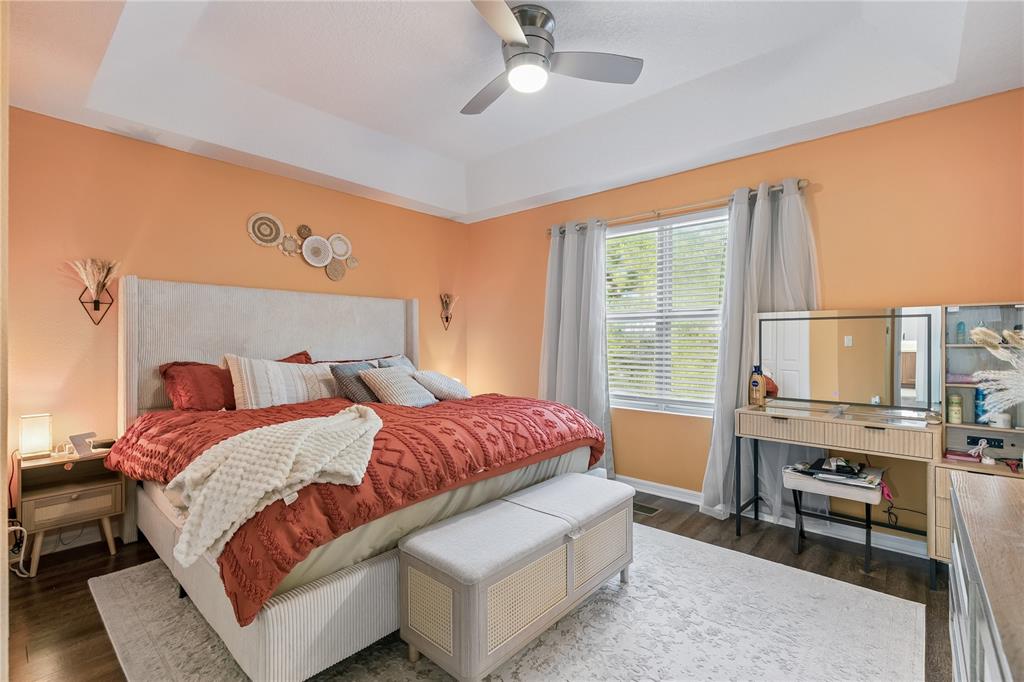A bedroom features peach walls, a tray ceiling, a bed with a textured quilt, and furniture — 2264 BETSY ROSS LANE UNIT 2264, ST CLOUD, FL
