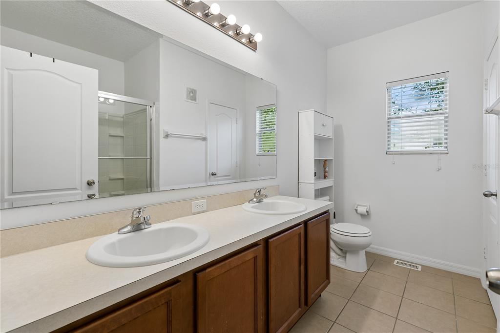 A bathroom features a double vanity with wood cabinets, a large mirror, and a toilet — 2264 BETSY ROSS LANE UNIT 2264, ST CLOUD, FL