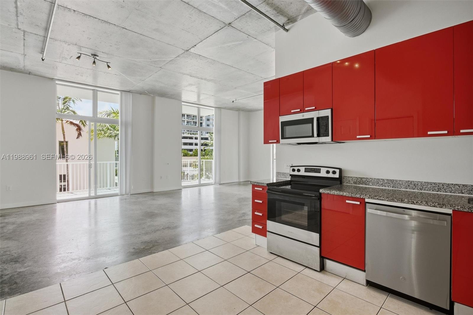 A kitchen with red cabinets and concrete ceilings opens into a bright living area — 2100 Van Buren St # 319, Hollywood FL 33020, HOLLYWOOD, FL