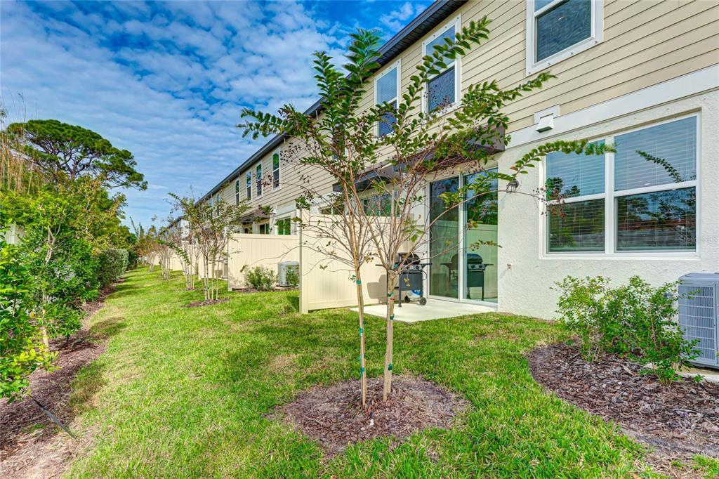 The exterior of a multi-unit townhouse features a grassy lawn, small trees, and privacy fences — 17063 CORAL KEY DRIVE, NOKOMIS, FL