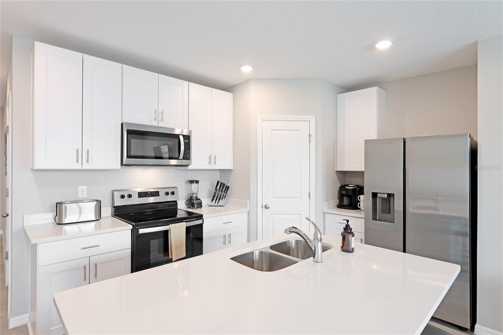 A modern kitchen features white cabinetry, stainless steel appliances, and a large white quartz island — 17063 CORAL KEY DRIVE, NOKOMIS, FL