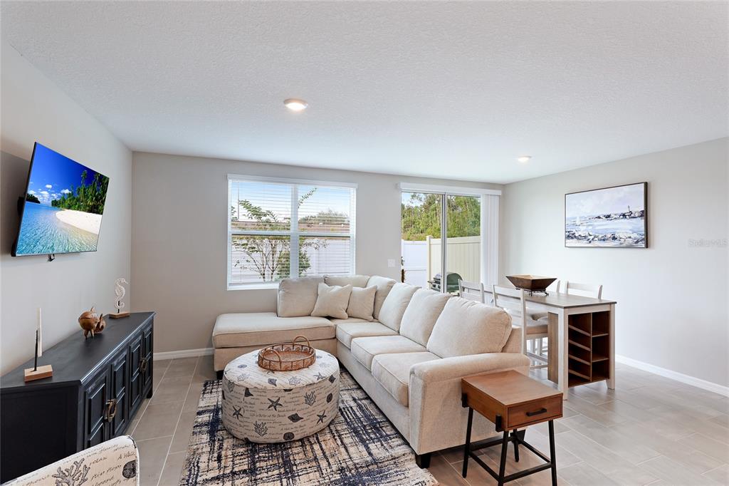 A living room with a sectional sofa, a round ottoman, a television, and a dining area — 17063 CORAL KEY DRIVE, NOKOMIS, FL