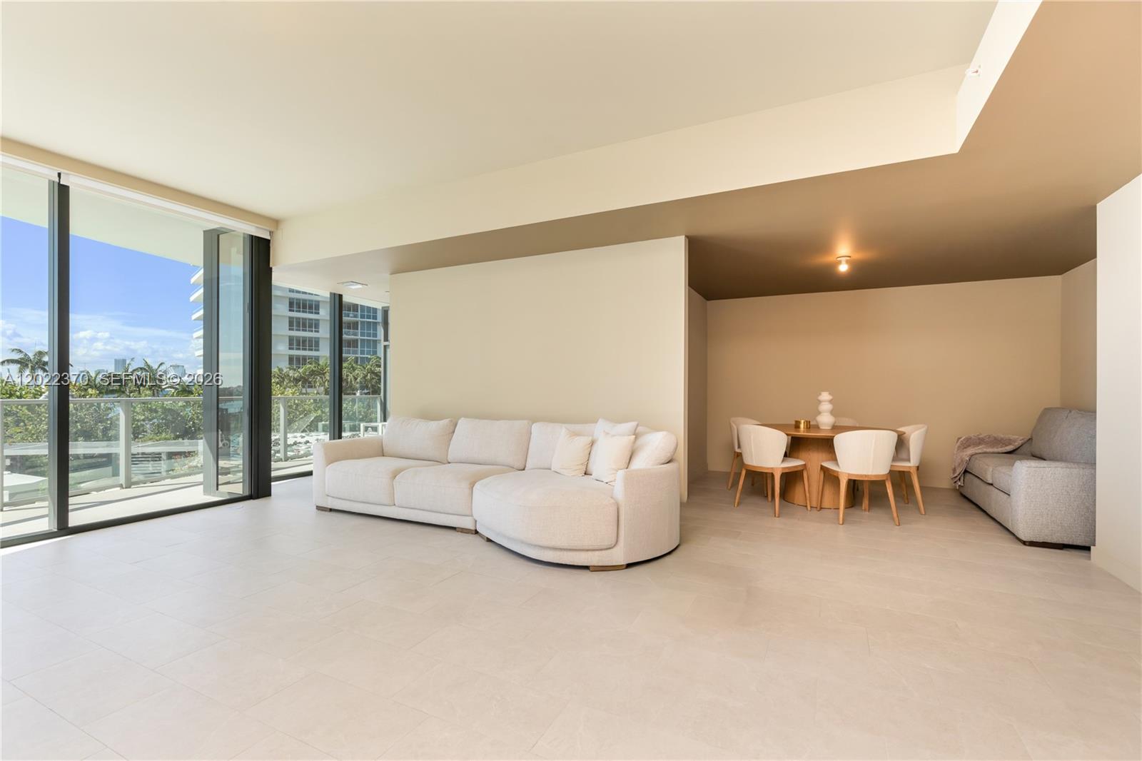 A modern living and dining area features light tile floors, a curved sofa, and floor-to-ceiling windows — 500 Alton Rd # 802, Miami Beach FL 33139, MIAMI BEACH, FL