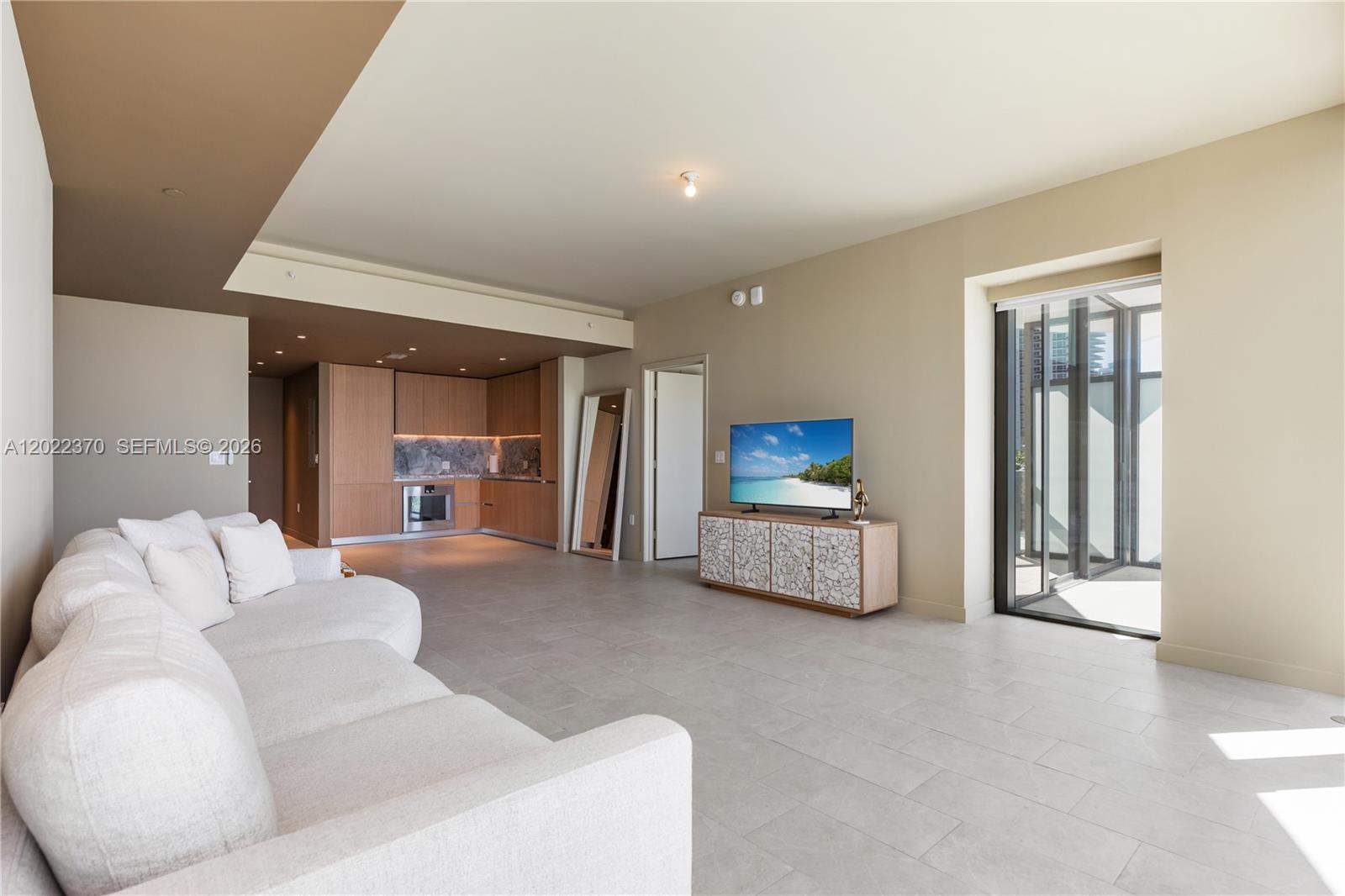 A modern living room features a white sofa, a television on a cabinet, and a kitchen — 500 Alton Rd # 802, Miami Beach FL 33139, MIAMI BEACH, FL