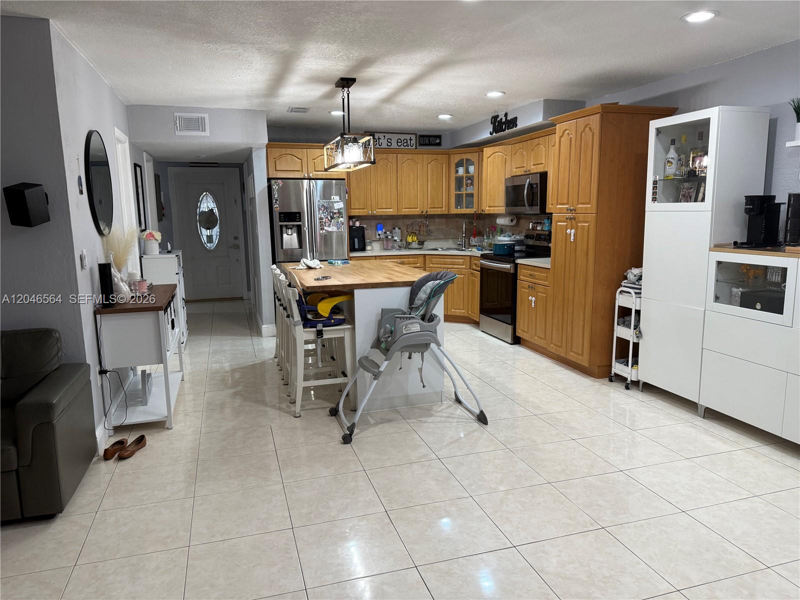 A kitchen features wood cabinets, a central island with bar seating, and light tile flooring — 7151 W 3rd Ct # 0, Hialeah FL 33014, HIALEAH, FL