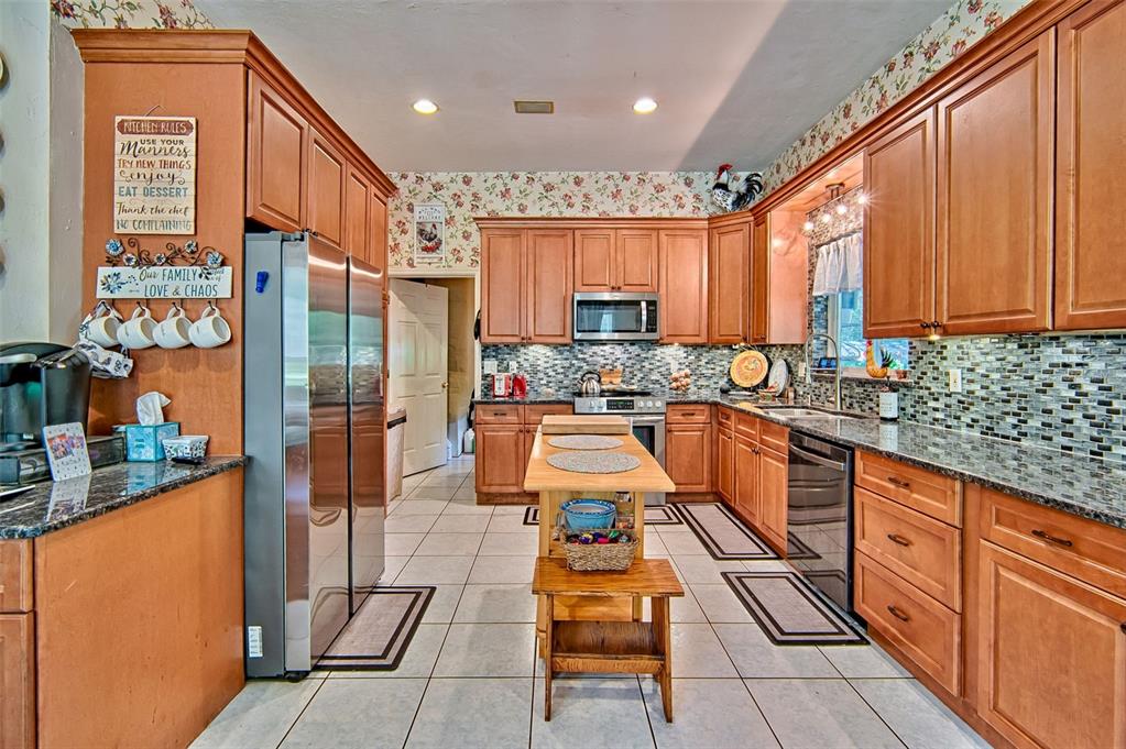 A kitchen features wood cabinets, granite countertops, a central island, and floral wallpaper — 15522 SW 75TH STREET, ARCHER, FL