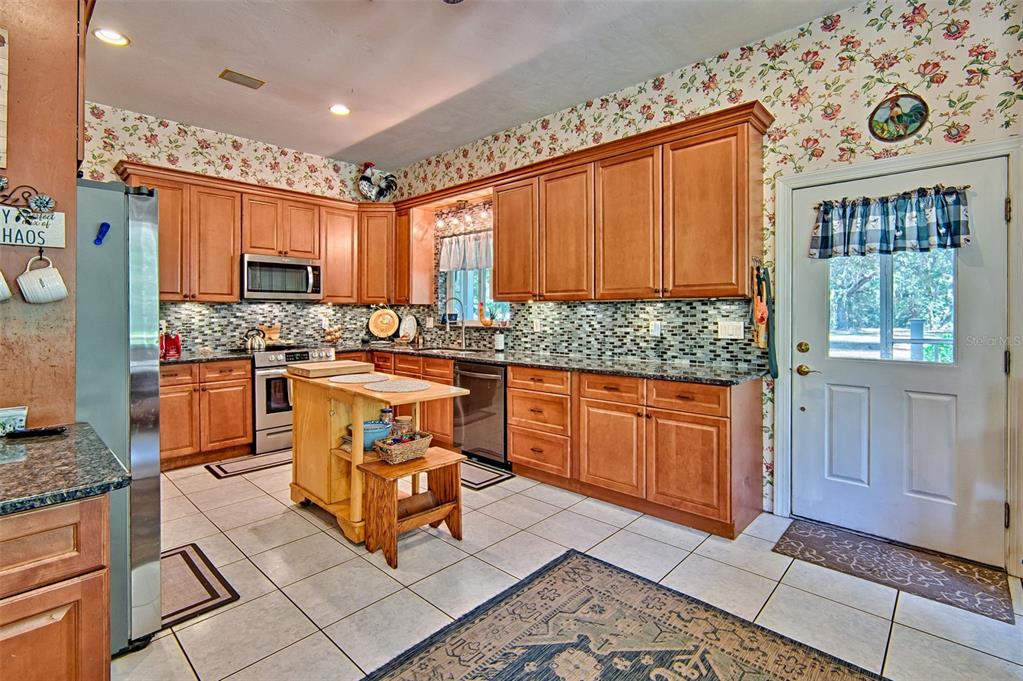 A kitchen features wood cabinets, granite countertops, a tile backsplash, and a small wooden island — 15522 SW 75TH STREET, ARCHER, FL