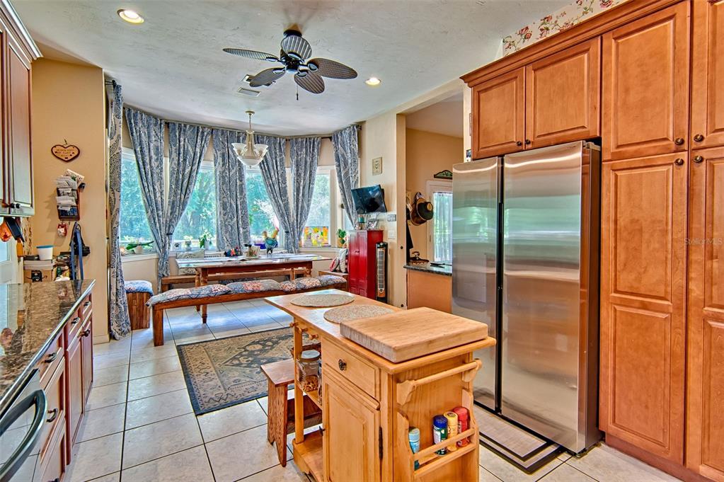 A kitchen features wooden cabinets, a stainless steel refrigerator, a center island, and a dining area — 15522 SW 75TH STREET, ARCHER, FL