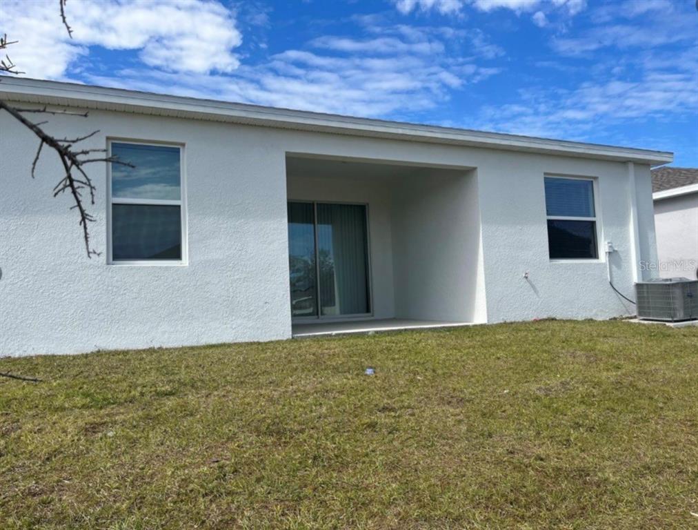 The exterior rear view of a white stucco house features a covered patio and lawn — 855 TURNER LANE, WINTER HAVEN, FL