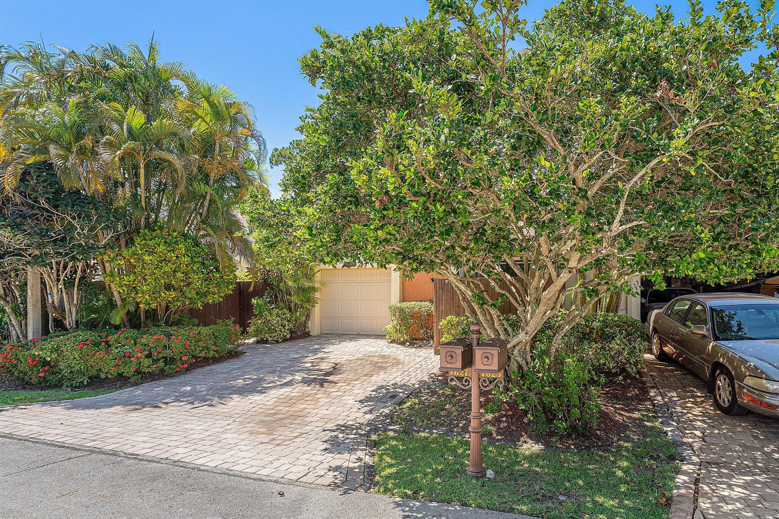 A paved driveway leads to a garage, shaded by a large tree and lush landscaping — 7627 Sierra Drive W, Boca Raton FL 33433, BOCA RATON, FL