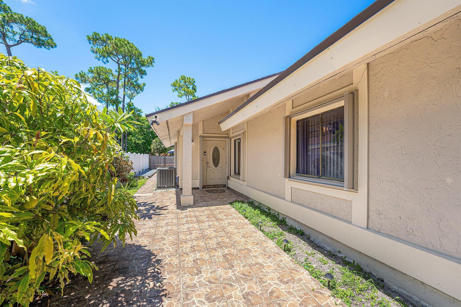 A tiled walkway leads to the front entrance of a beige house with a window — 7627 Sierra Drive W, Boca Raton FL 33433, BOCA RATON, FL