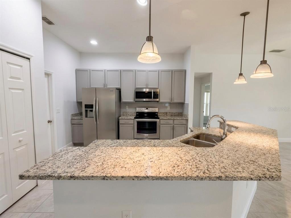 A kitchen features gray cabinets, stainless steel appliances, and a granite-topped peninsula with a sink — 3133 RIACHUELO LANE, KISSIMMEE, FL