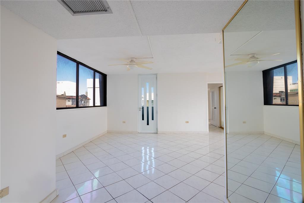 A bright, empty room features white tiled floors, a ceiling fan, and a mirrored wall — 610 AVE. MIRAMAR UNIT 5-B, SAN JUAN, PR