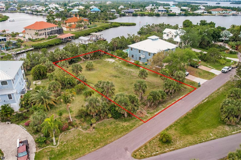 An aerial view shows a vacant, rectangular residential lot outlined in red near a waterway — 24169 JOLLY ROGER BOULEVARD, PUNTA GORDA, FL