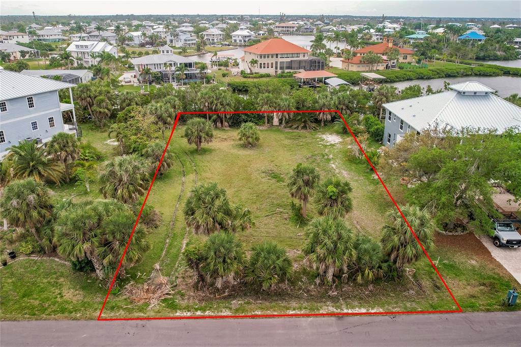 An aerial view shows a vacant, rectangular residential lot outlined in red near a waterway — 24169 JOLLY ROGER BOULEVARD, PUNTA GORDA, FL