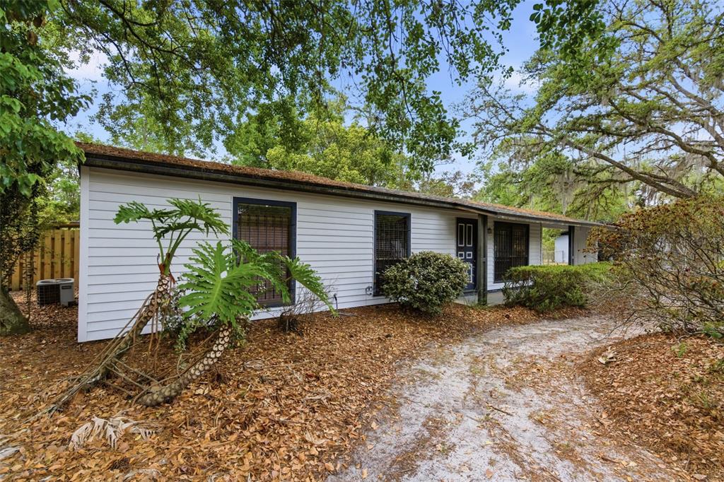 A white single-story house with dark trim sits on a sandy lot with mature trees — 2849 NW 57TH PLACE, GAINESVILLE, FL