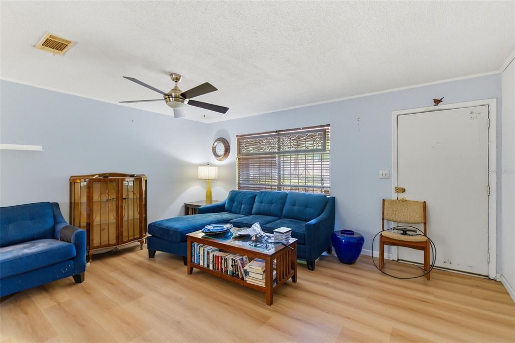 A living room features light blue walls, wood-look flooring, a blue sectional, and a ceiling fan — 2849 NW 57TH PLACE, GAINESVILLE, FL