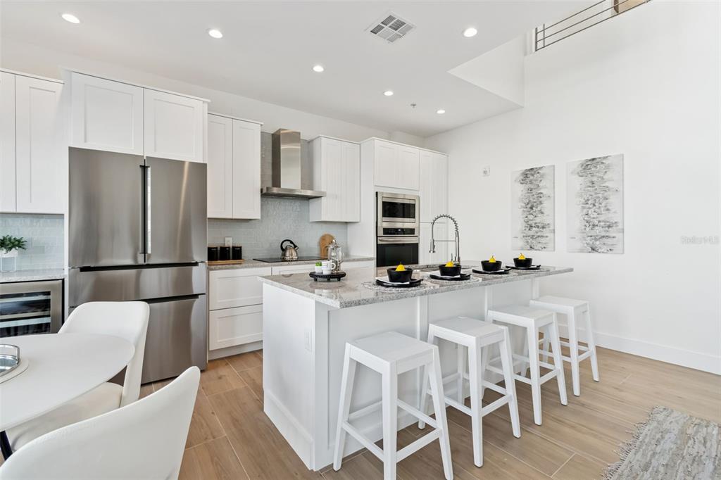 A modern kitchen features white cabinetry, stainless steel appliances, a granite island, and a dining area — 1343 4TH STREET UNIT 202, SARASOTA, FL