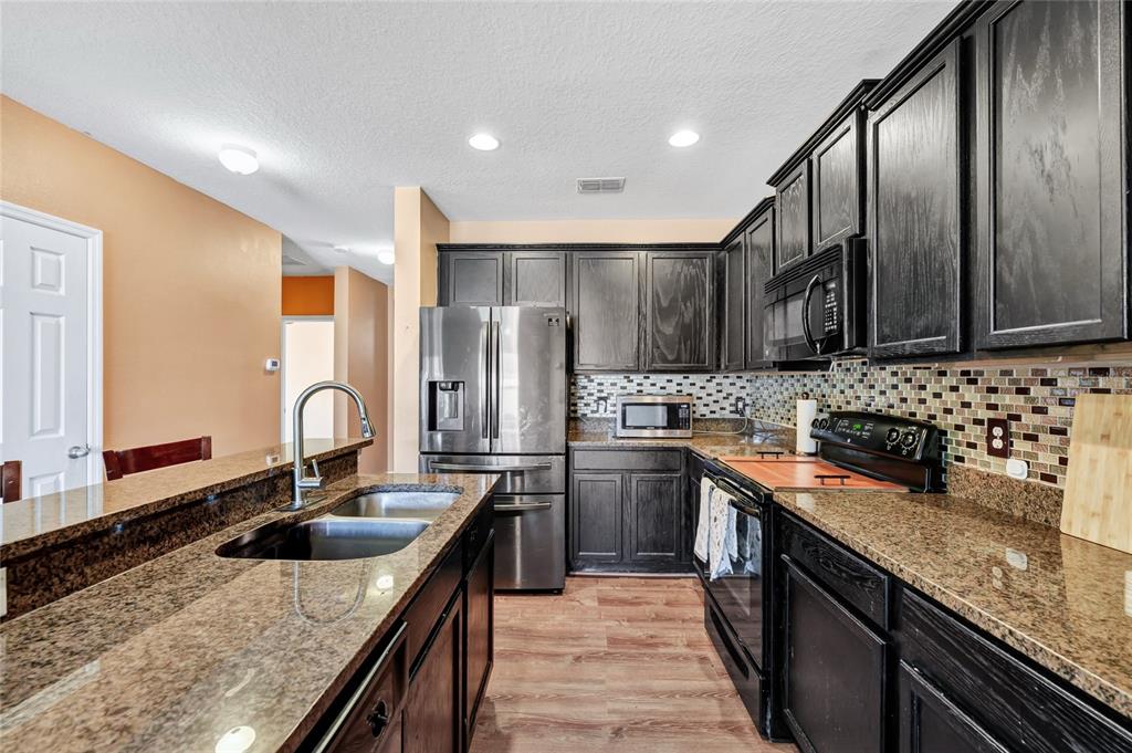 A kitchen features dark wood cabinets, granite countertops, stainless steel appliances, and a tiled backsplash — 4607 KALISPELL ROAD, KISSIMMEE, FL