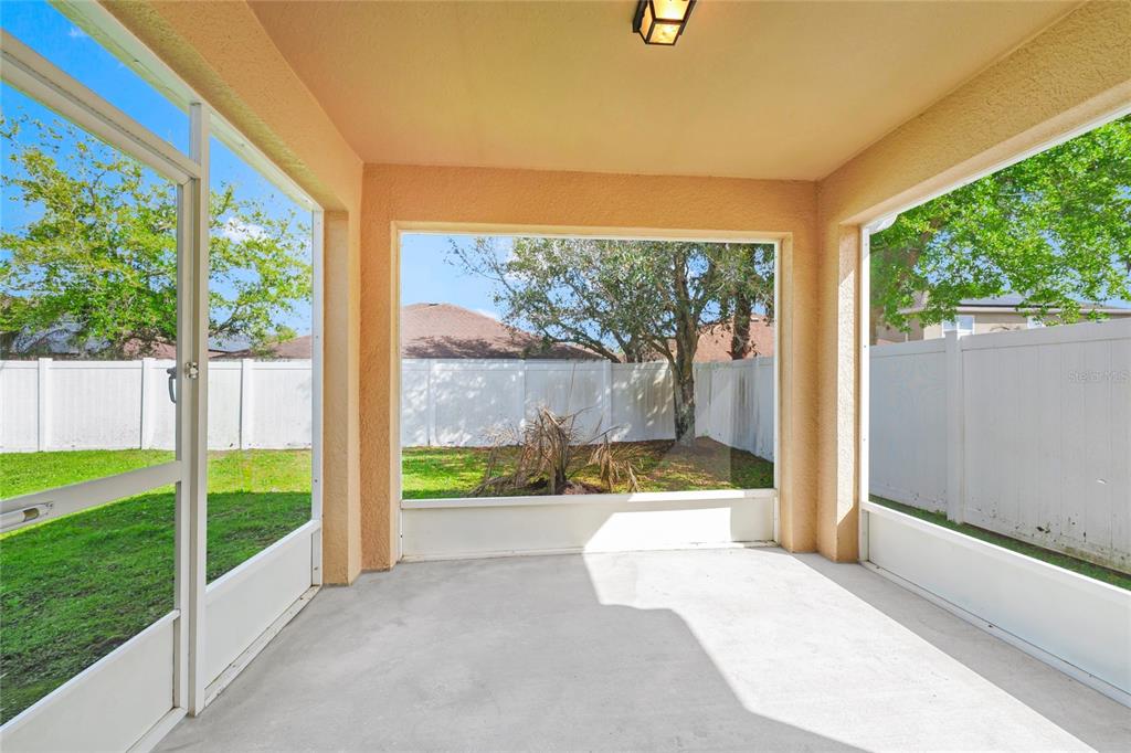 A screened-in concrete patio overlooks a fenced backyard with trees and grass — 4607 KALISPELL ROAD, KISSIMMEE, FL