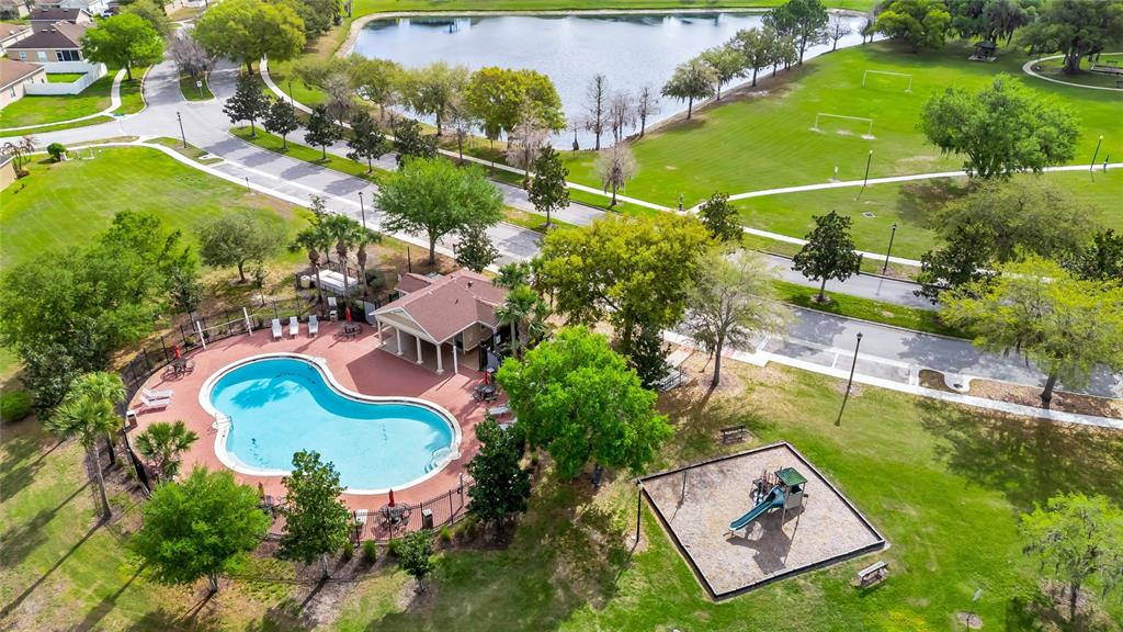 An aerial view shows a community swimming pool, clubhouse, and playground next to a lake — 4607 KALISPELL ROAD, KISSIMMEE, FL