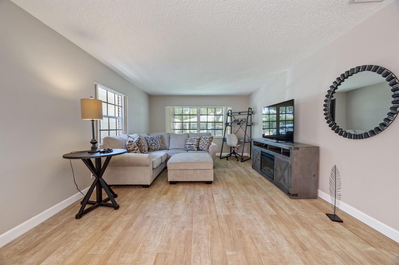 A living room features light wood-look tile flooring, a gray sectional sofa, and a television console — 10168 43rd Trail S # 318, Boynton Beach FL 33436, BOYNTON BEACH, FL