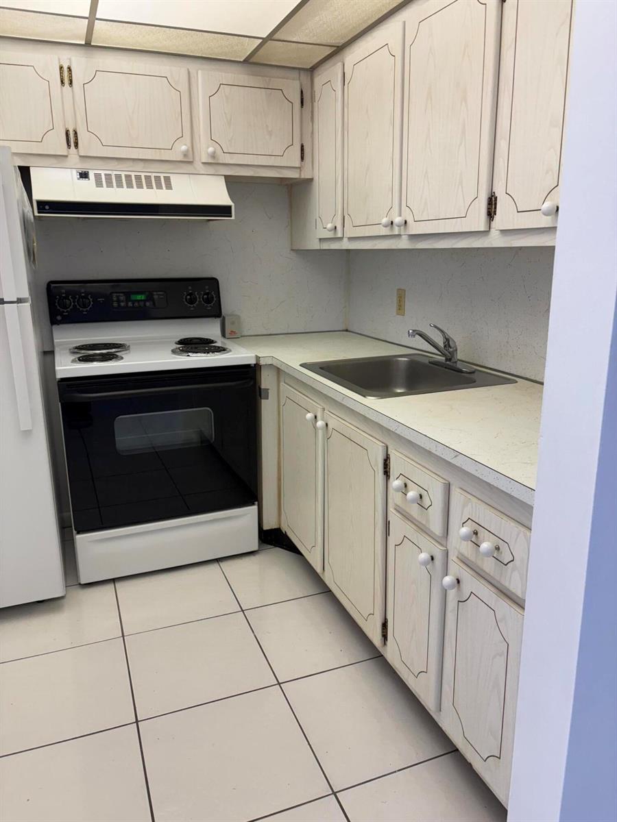 A small kitchen features white cabinets, a white stove, a stainless steel sink, and tiled floors — 113 Berkshire E, West Palm Beach FL 33417, WEST PALM BEACH, FL