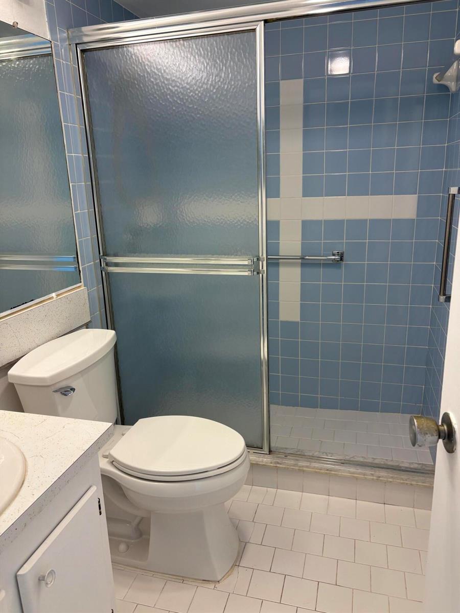 A bathroom features a white toilet, a vanity, and a shower with blue tiled walls — 113 Berkshire E, West Palm Beach FL 33417, WEST PALM BEACH, FL
