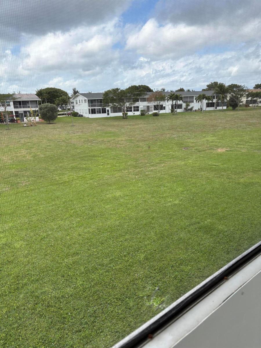 A view of a large grassy lawn and residential buildings seen through a window screen — 113 Berkshire E, West Palm Beach FL 33417, WEST PALM BEACH, FL