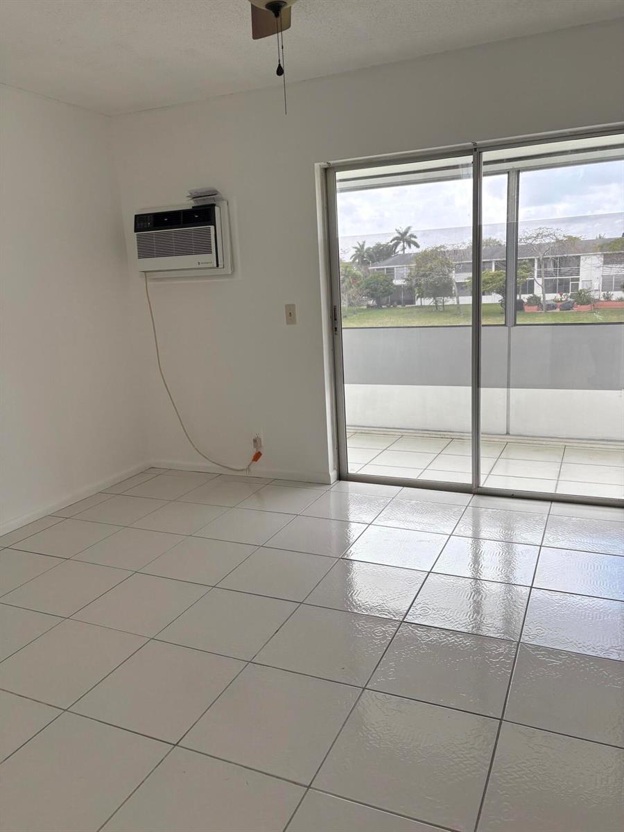 An empty room with white tile floors, a wall-mounted air conditioner, and a sliding glass door — 113 Berkshire E, West Palm Beach FL 33417, WEST PALM BEACH, FL