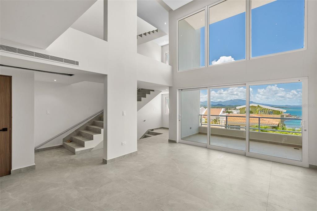 A modern, high-ceilinged living room with tile floors, a staircase, and large sliding glass doors — . SHELL CASTLE CLUB UNIT 46, HUMACAO, PR