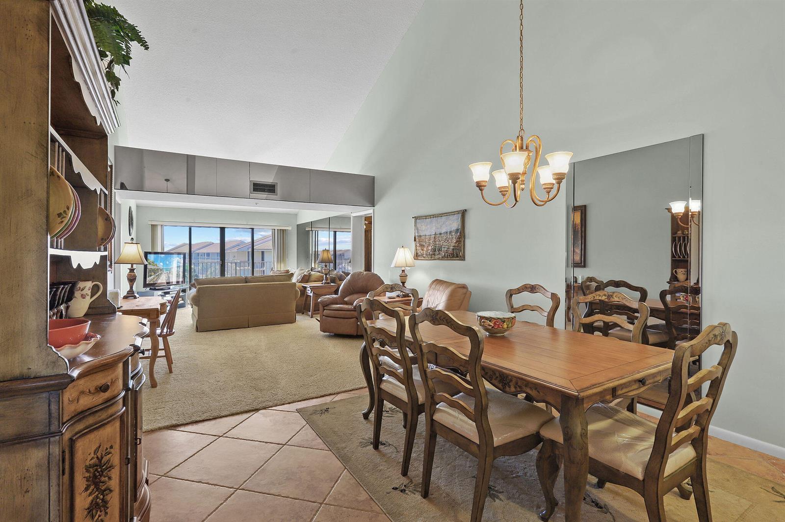 A dining area with a wooden table and chairs sits adjacent to a carpeted living room — 1601 Marina Isle Way # 505, Jupiter FL 33477, JUPITER, FL
