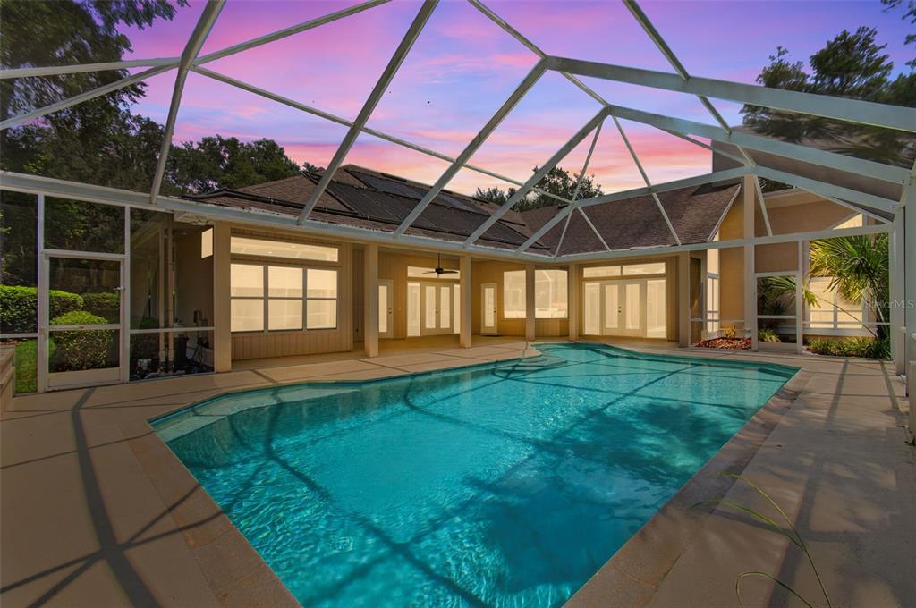 A swimming pool is enclosed by a screened lanai attached to the back of a house — 9227 SW 43RD LANE, GAINESVILLE, FL