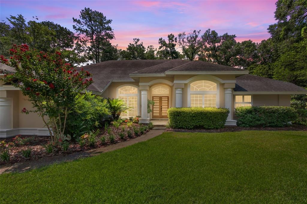 A single-story house with a beige stucco exterior, arched windows, and a front lawn at dusk — 9227 SW 43RD LANE, GAINESVILLE, FL