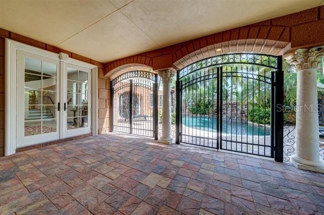 A covered stone patio features arched iron gates opening to a swimming pool area — 829 BRUCE AVENUE, CLEARWATER BEACH, FL