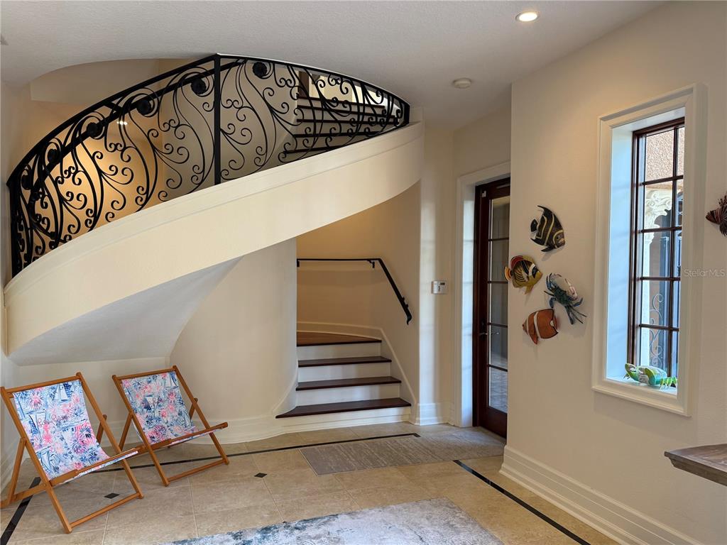 A foyer features a curved staircase with wrought iron railings, tile flooring, and beach-themed decor — 829 BRUCE AVENUE, CLEARWATER BEACH, FL