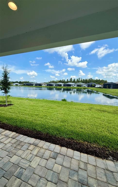 A paved patio overlooks a grassy lawn and a pond with houses in the distance — 3419 MALTA AVENUE, WESLEY CHAPEL, FL