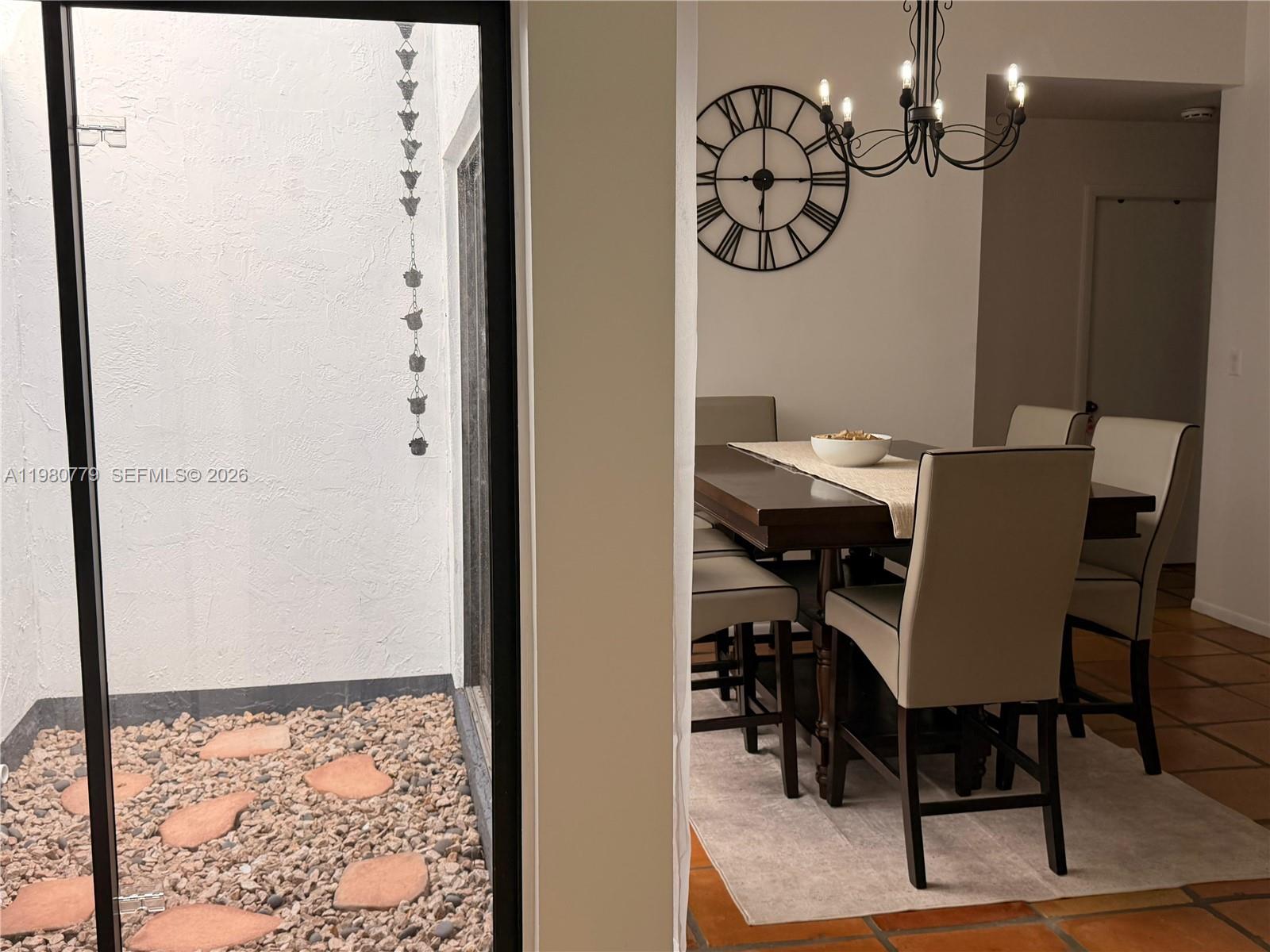 A dining room with a chandelier and large wall clock overlooks an outdoor rock garden — 6641 NW 174th Ter, Hialeah FL 33015, HIALEAH, FL