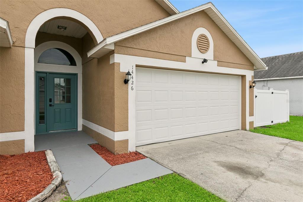 The exterior of a tan house features a white garage door and a teal front door — 14426 LAKE PRICE DRIVE, ORLANDO, FL