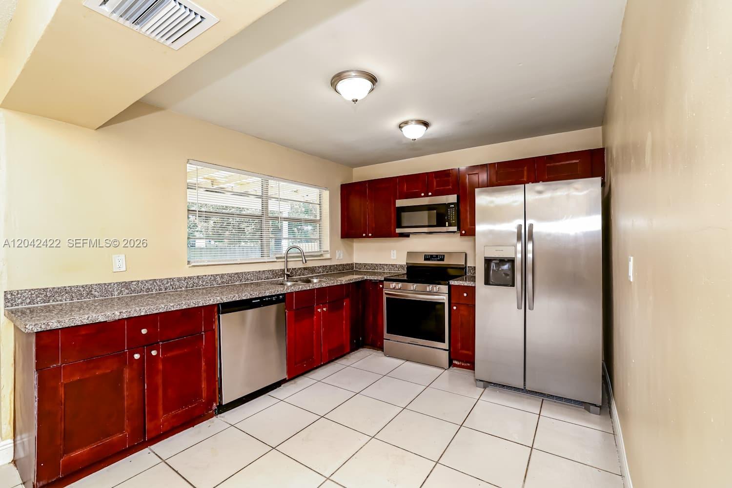 A kitchen features dark wood cabinets, stainless steel appliances, granite countertops, and white tile flooring — BOYNTON BEACH, FL