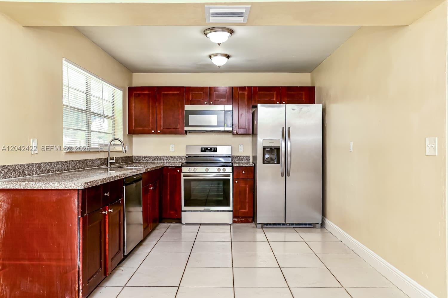 A kitchen features dark wood cabinets, stainless steel appliances, granite countertops, and light tile flooring — BOYNTON BEACH, FL