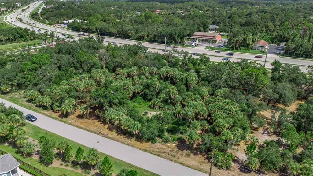 An aerial view shows a wooded, undeveloped lot situated between a road and a highway — 16220 FRANKLIN AVENUE, PORT CHARLOTTE, FL