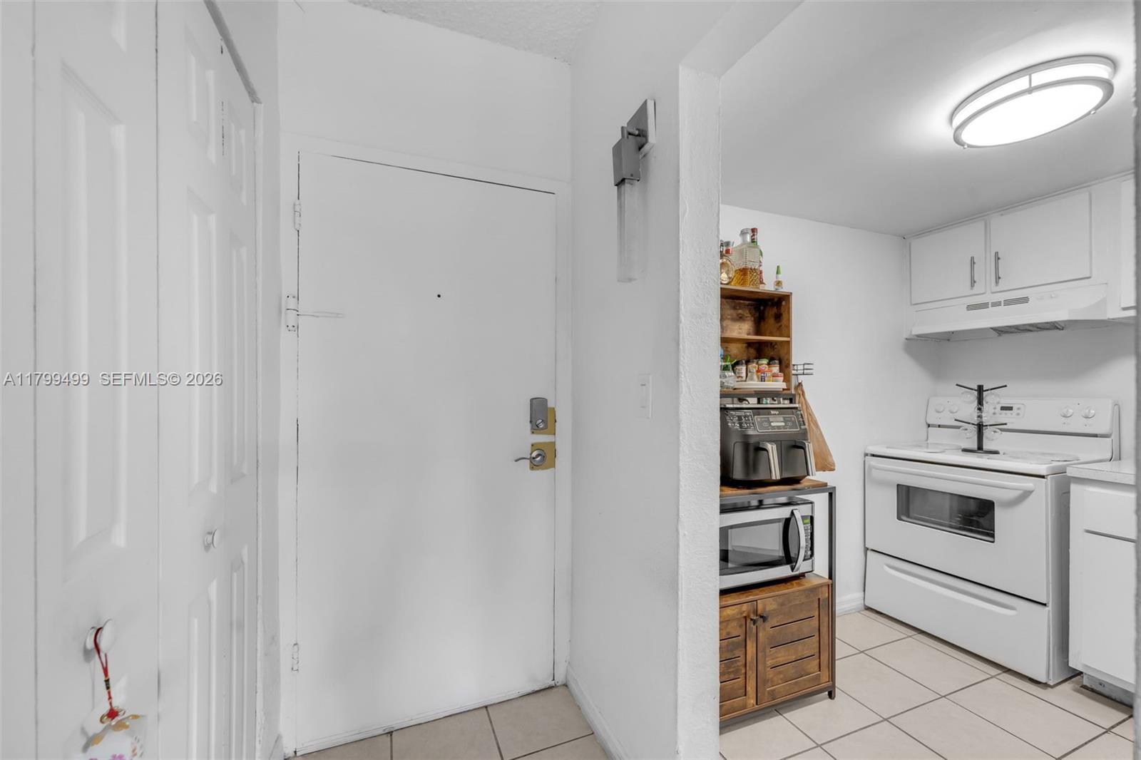 A white front door opens into a kitchen area with white cabinets and tile flooring — 4550 NW 9th St # 106E, Miami FL 33126, MIAMI, FL
