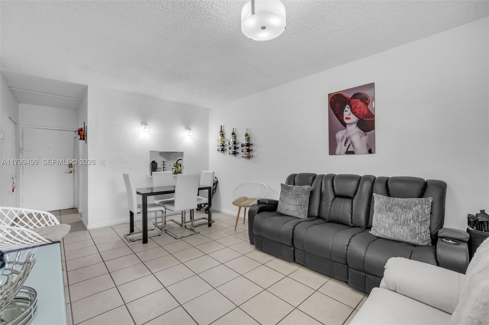 A living and dining area features white tile floors, a black sofa, and wall-mounted wine racks — 4550 NW 9th St # 106E, Miami FL 33126, MIAMI, FL