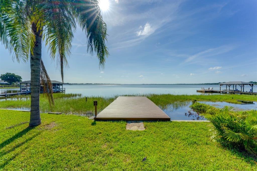 A wooden dock extends from a grassy lawn into a lake under a sunny sky — 900 N HARBOR TERRACE, TAVARES, FL