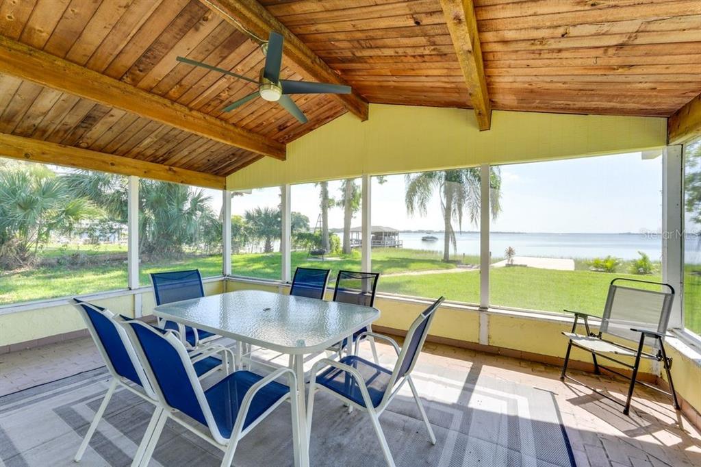 A screened-in porch features a dining set, a ceiling fan, and views of a lake — 900 N HARBOR TERRACE, TAVARES, FL