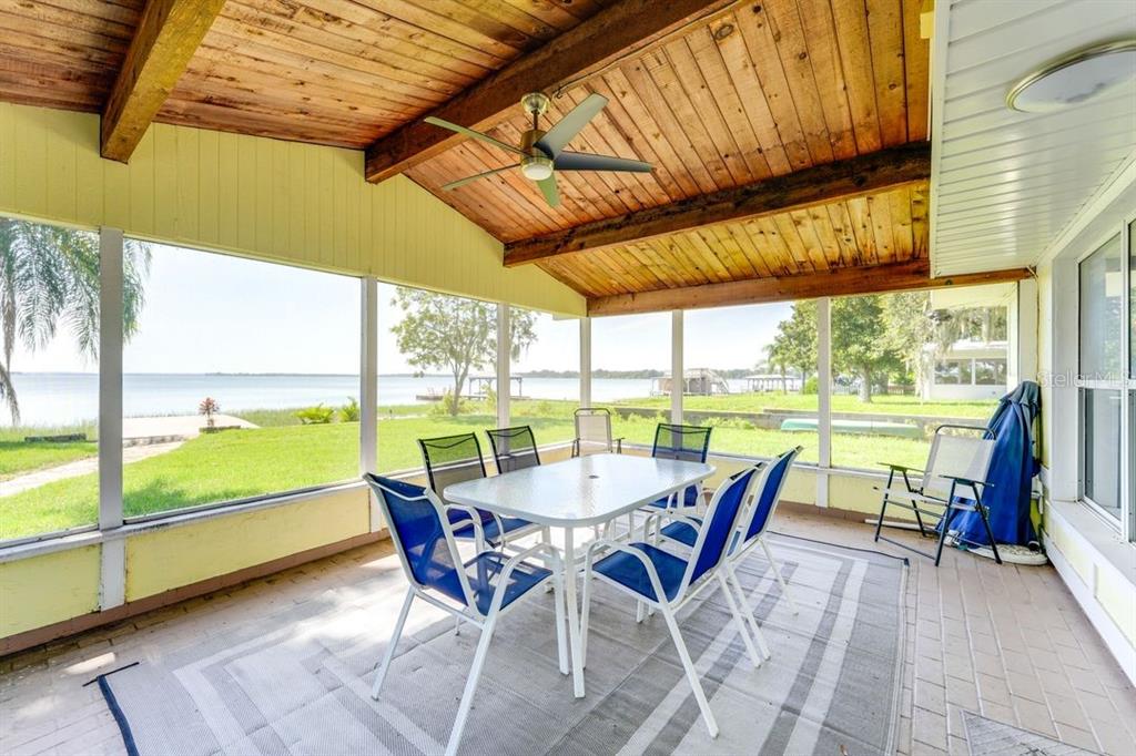 A screened-in porch with a wood-paneled ceiling, dining set, and a view of the lake — 900 N HARBOR TERRACE, TAVARES, FL