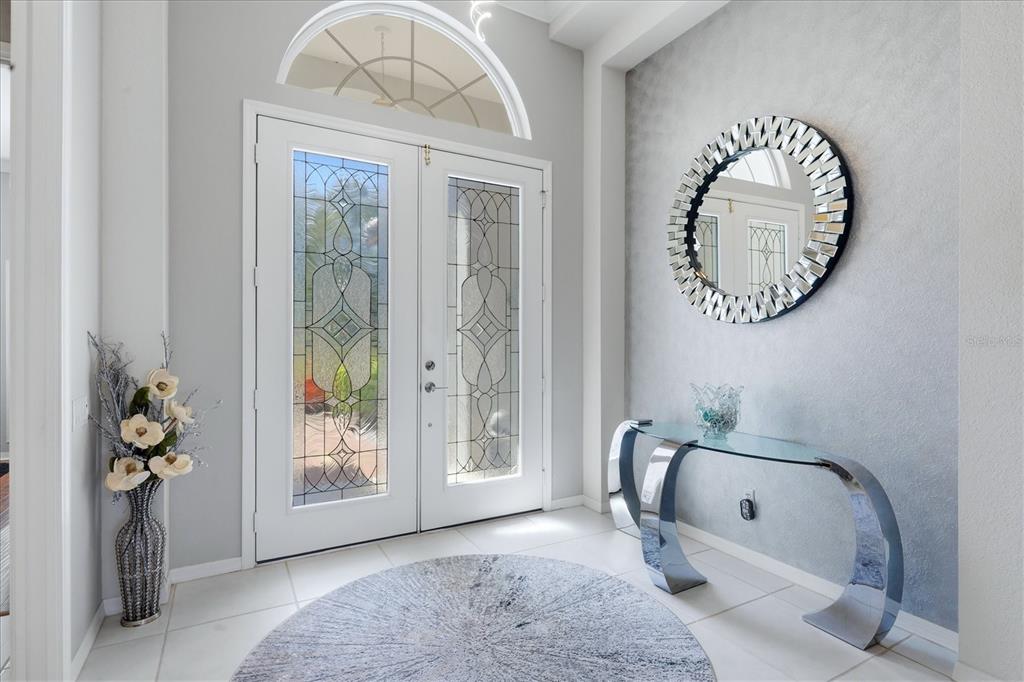 A bright entryway features double glass-paneled doors, a round mirror, and a modern console table — 7346 WINDEMERE LANE, UNIVERSITY PARK, FL